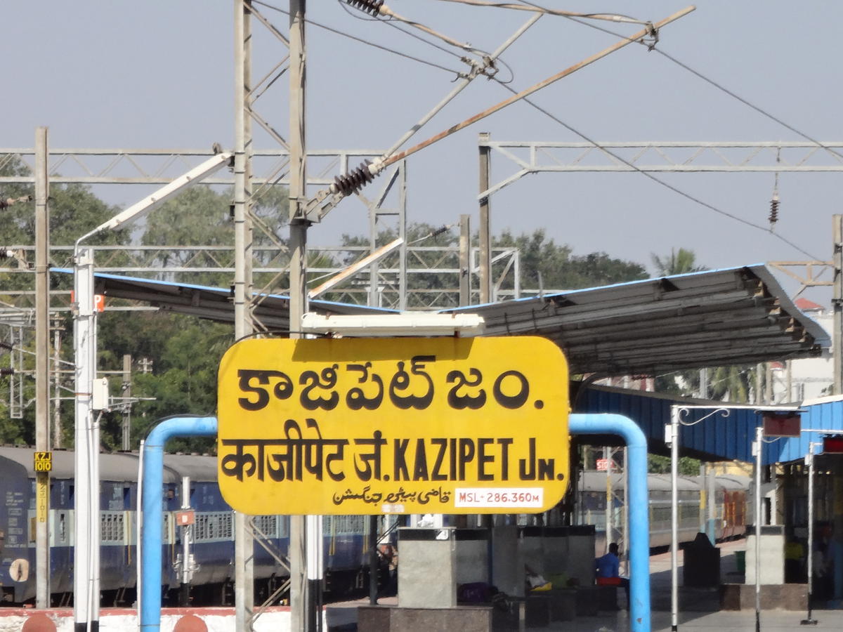 Kazipet Junction railway station signboard close-up with train and overhead electric lines