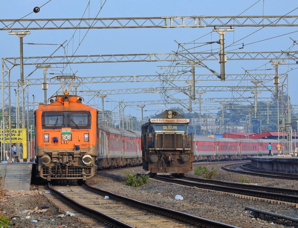 Indian Railways electric locomotive with passenger train and goods train on parallel tracks at railway station