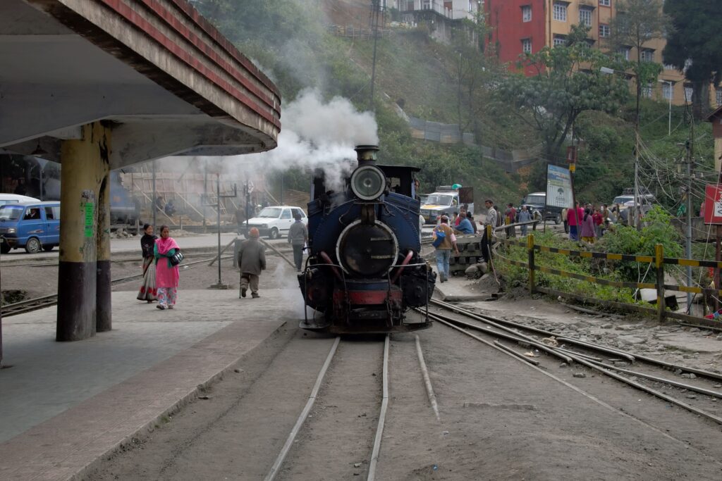 Steam locomotive toy train at hill station platform with passengers and tracks visible