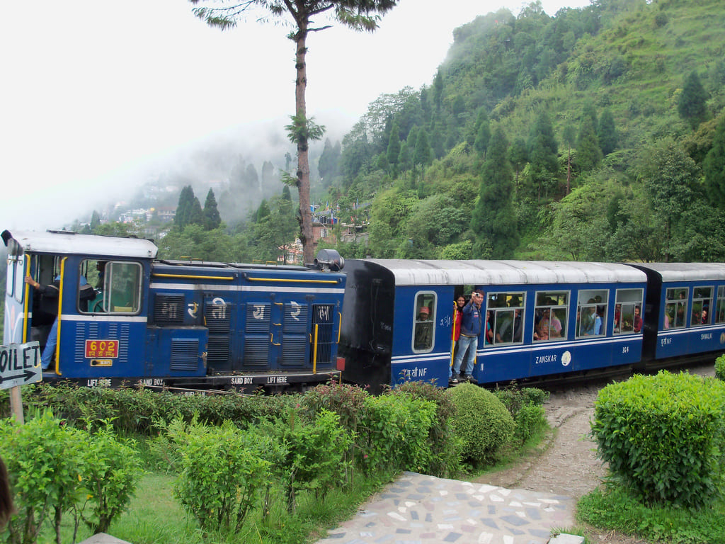 Darjeeling Himalayan Railway toy train passing through misty green hills with passengers onboard