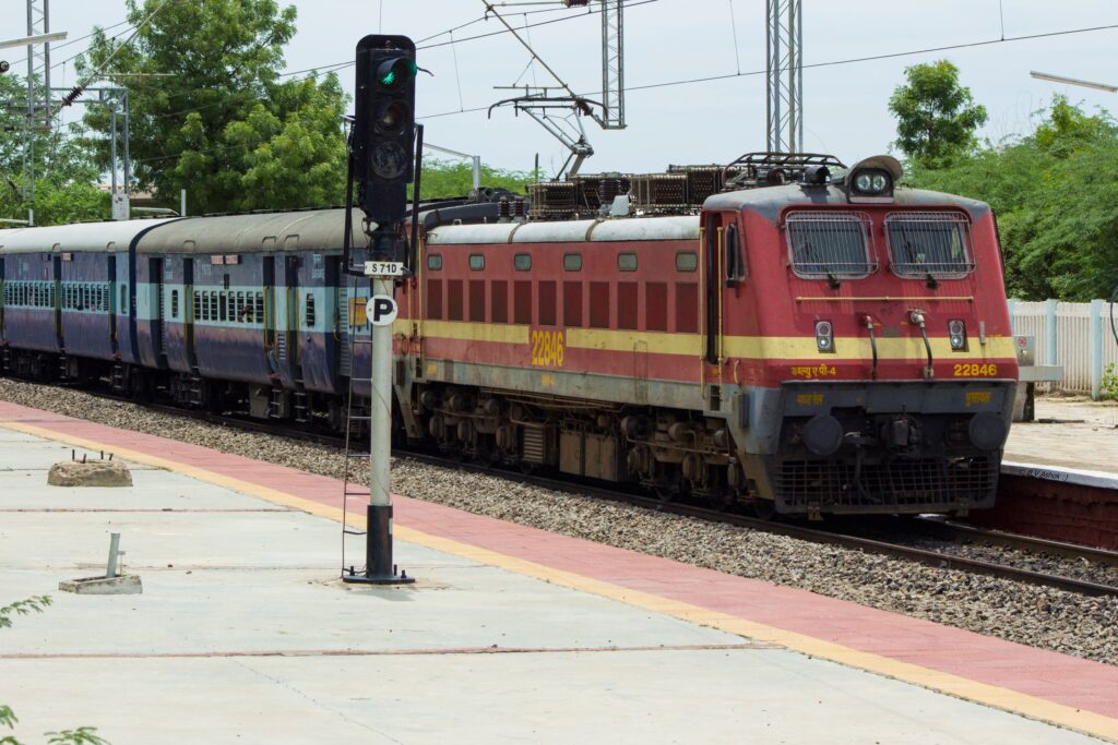 Indian Railways electric locomotive hauling passenger train at station with signal showing green