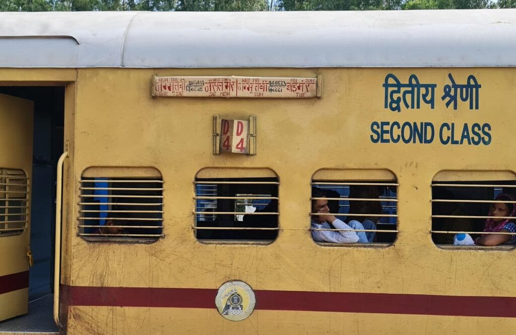 Indian Railways second class coach with passengers visible through barred windows