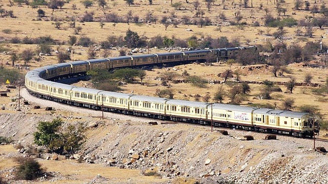 Indian passenger train curving through desert landscape in Rajasthan with long route and multiple coaches