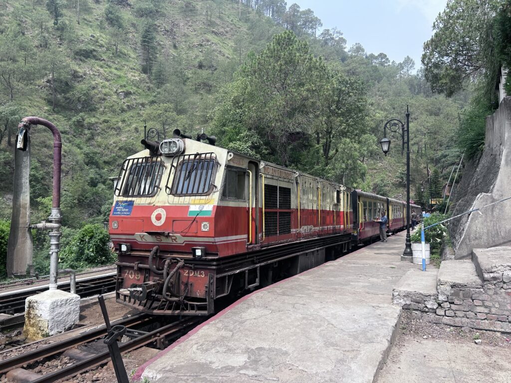 Mountain railway train at hill station platform surrounded by greenery and forested hills