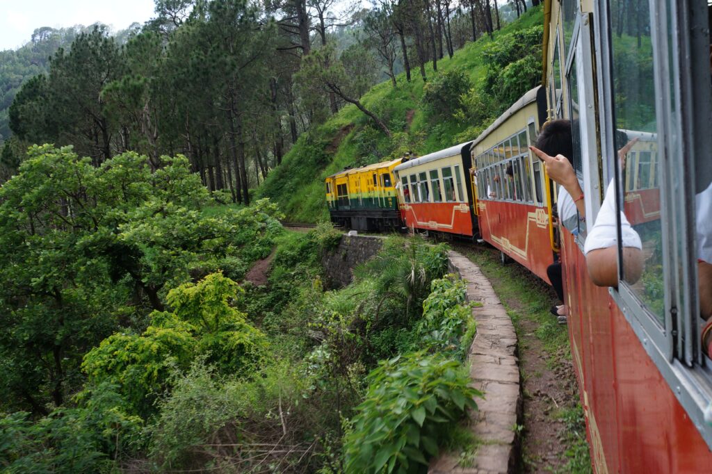Toy train moving along a narrow mountain track through dense green forest with sharp curves in India