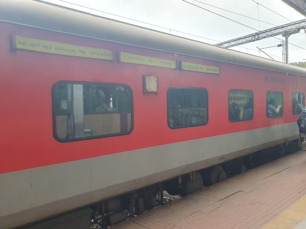 Indian Railways red coach train standing at platform during daytime with long distance route signage
