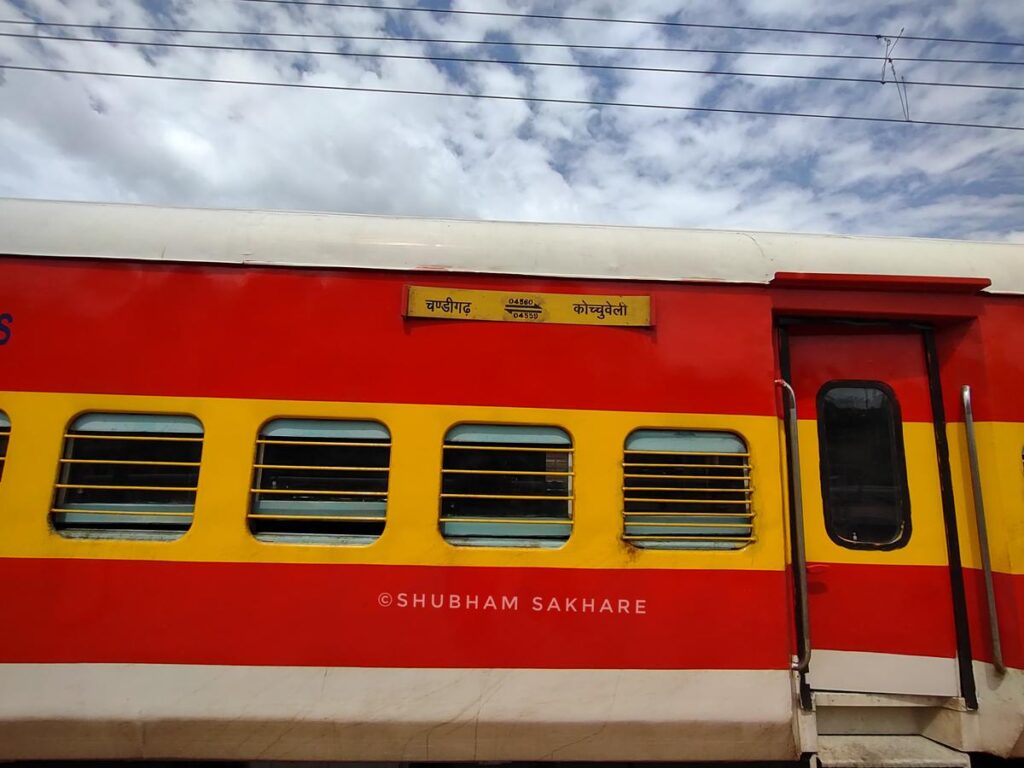 Indian Railways red and yellow sleeper class coach with barred windows at station