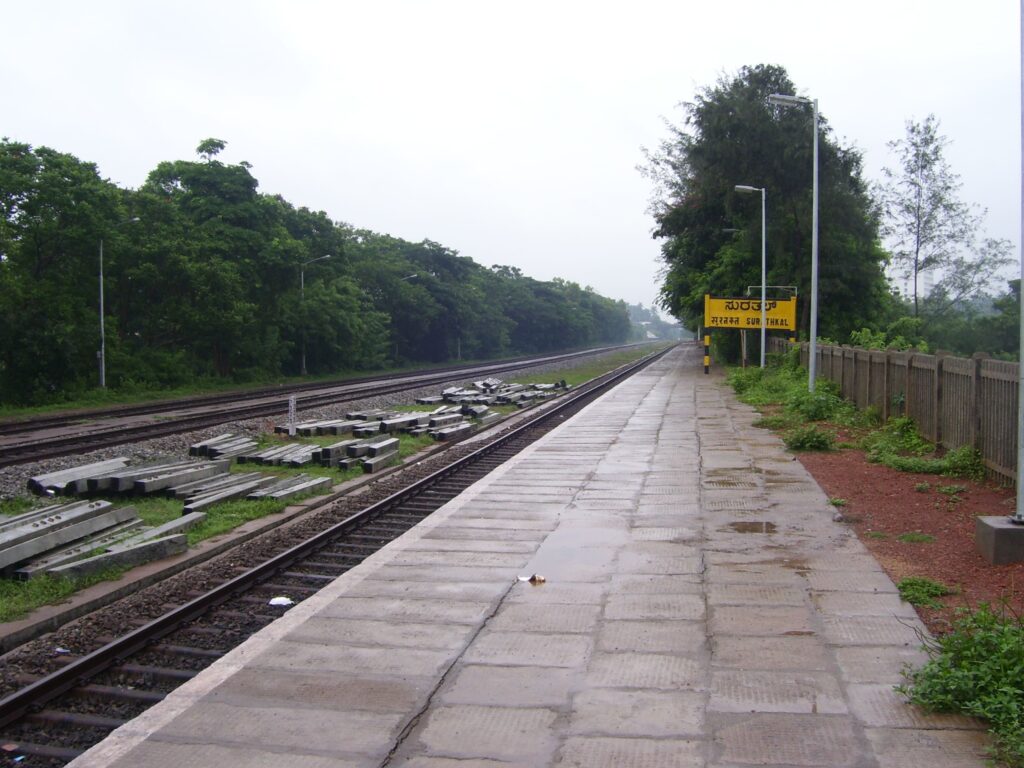 Surathkal railway station platform with tracks, greenery, and empty surroundings during monsoon