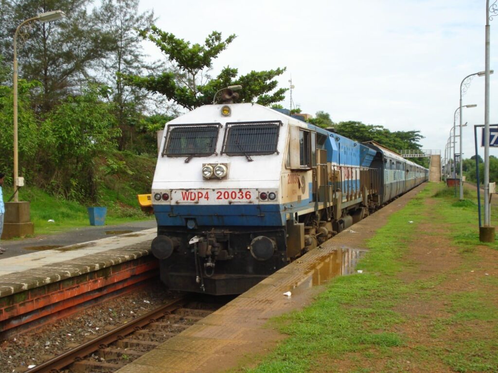 Indian Railways WDP4 diesel locomotive pulling a passenger train at a small station platform