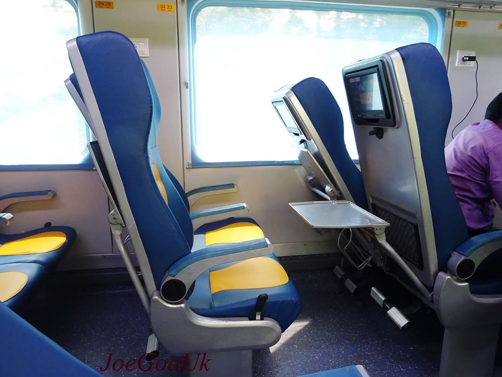 Modern train seats with tray tables and screens inside an Indian Railways coach
