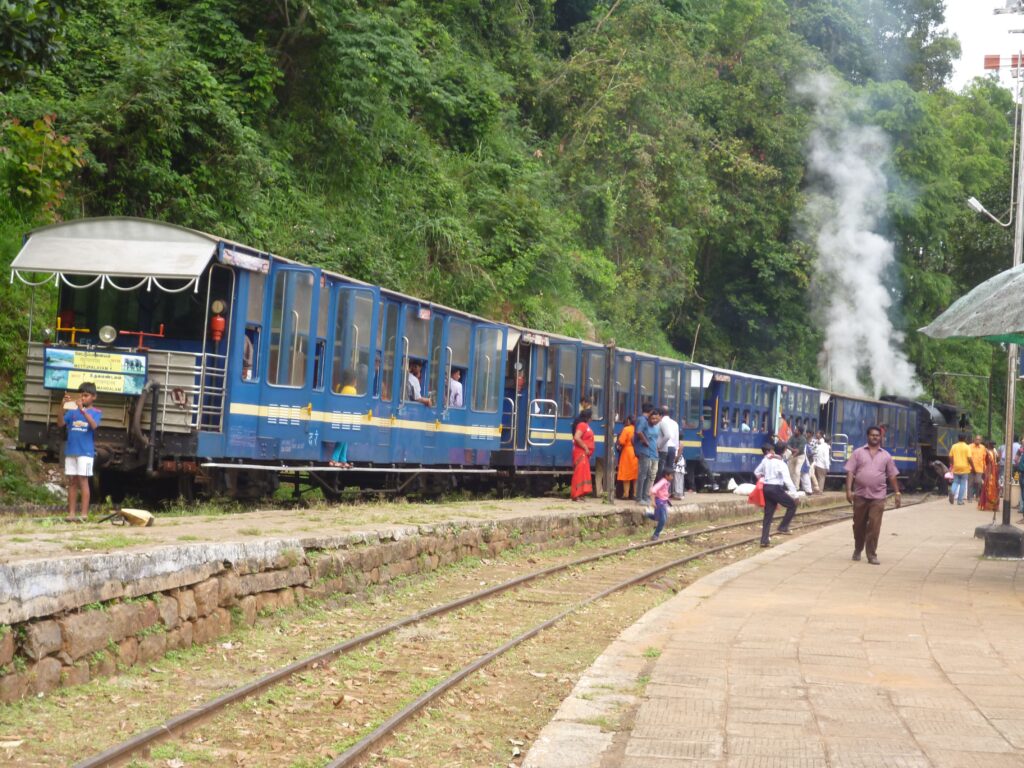 Blue toy train at hill station platform with passengers and steam engine in forested area