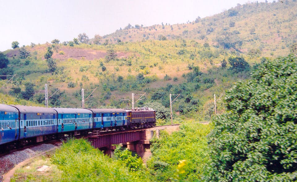 Indian Railways train crossing bridge through green hills and scenic countryside